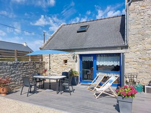 A stone building with a blue door, outdoor seating, and a wooden deck.