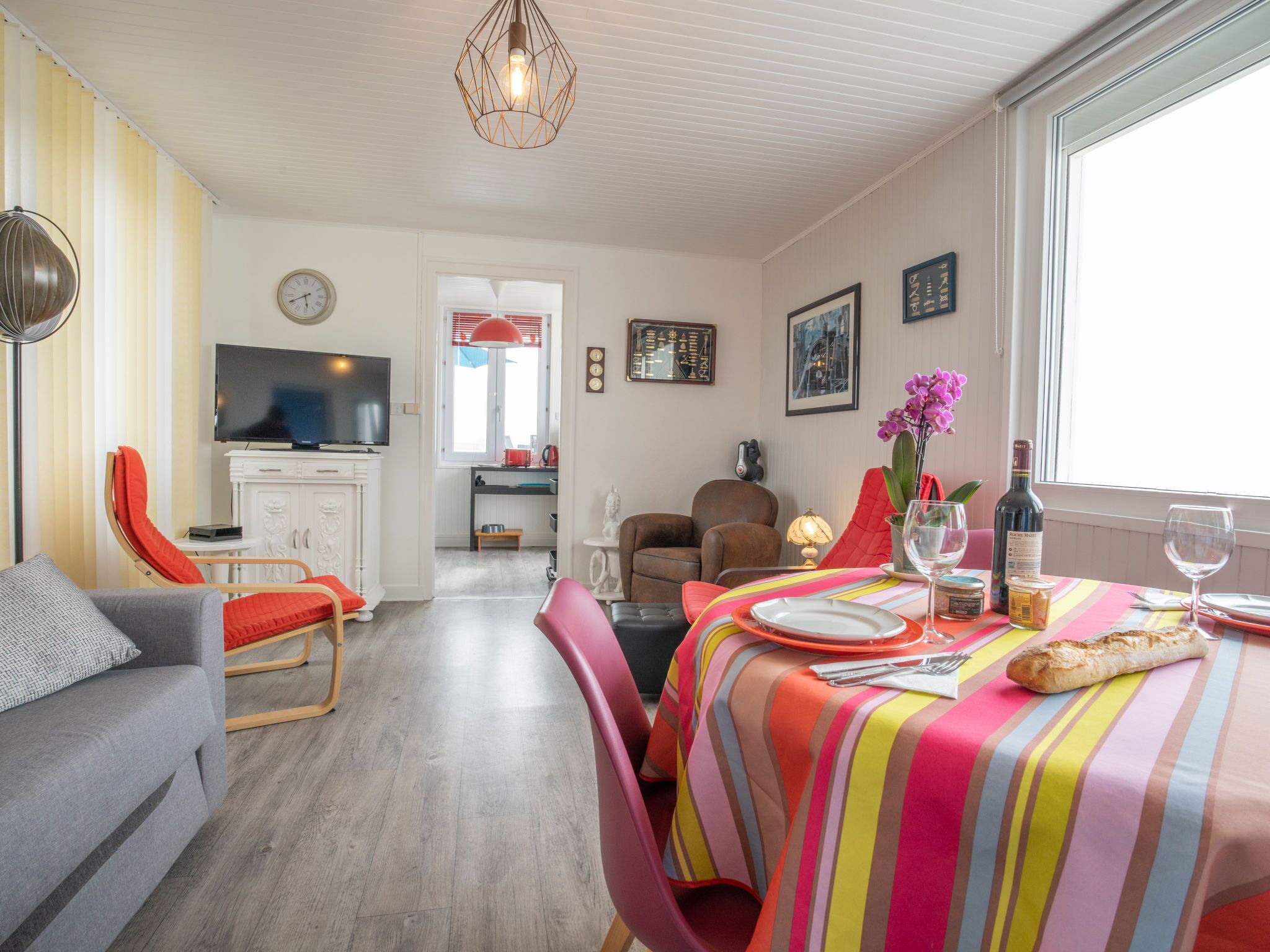 A compact living space with a dining area, a television, and a kitchen in the background.