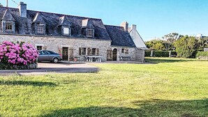 A stone house with a car parked in front, a grassy yard, and a flower bed with pink flowers. - Ker Iliav by Interhome (Plouescat)