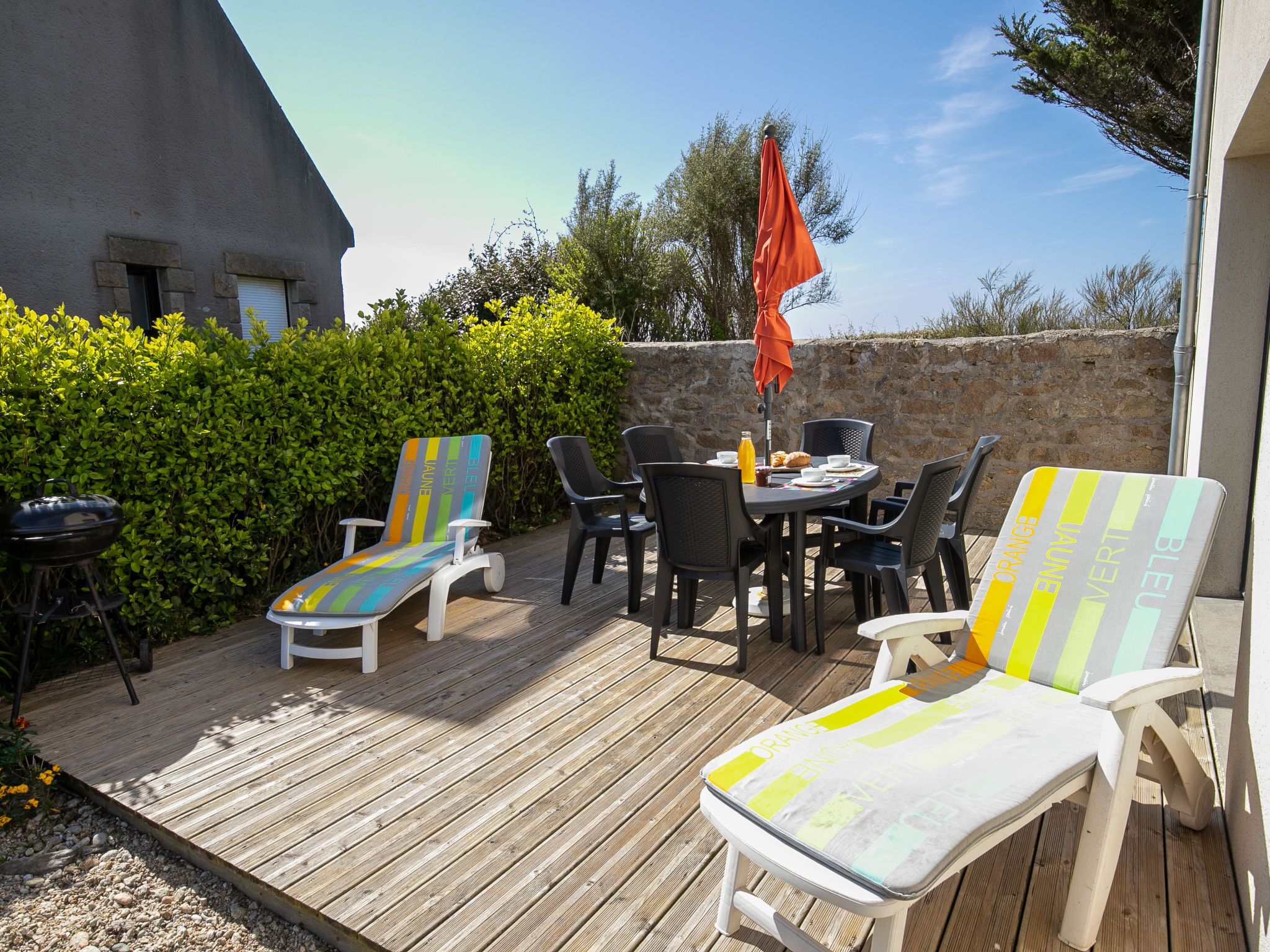 Una terrazza esterna con un pavimento in legno, poltrone da relax, un tavolo con sedie e un barbecue.