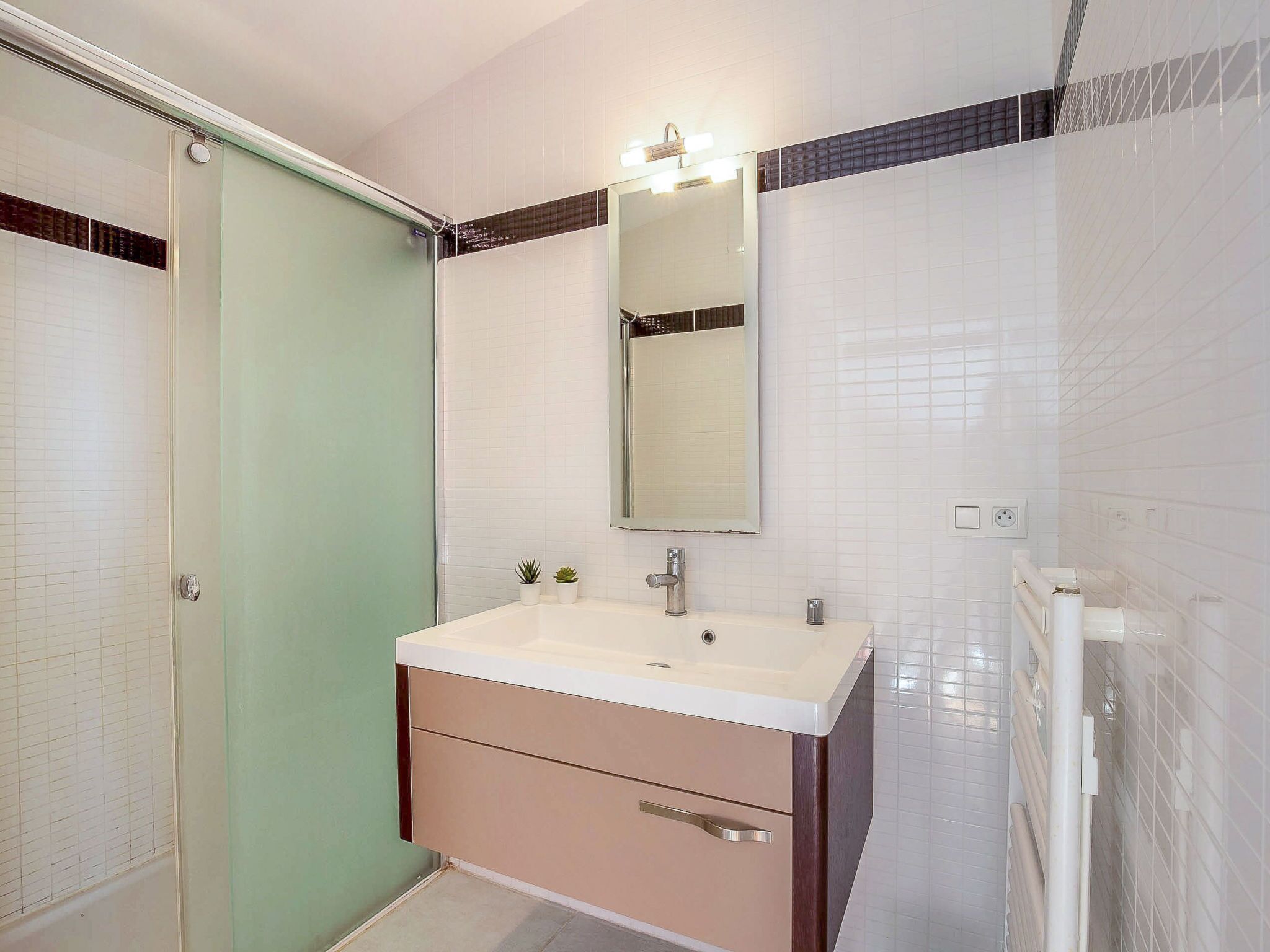 Une salle de bain moderne avec une douche à parois de verre, un lavabo blanc avec un miroir au-dessus et un meuble-lavabo beige.