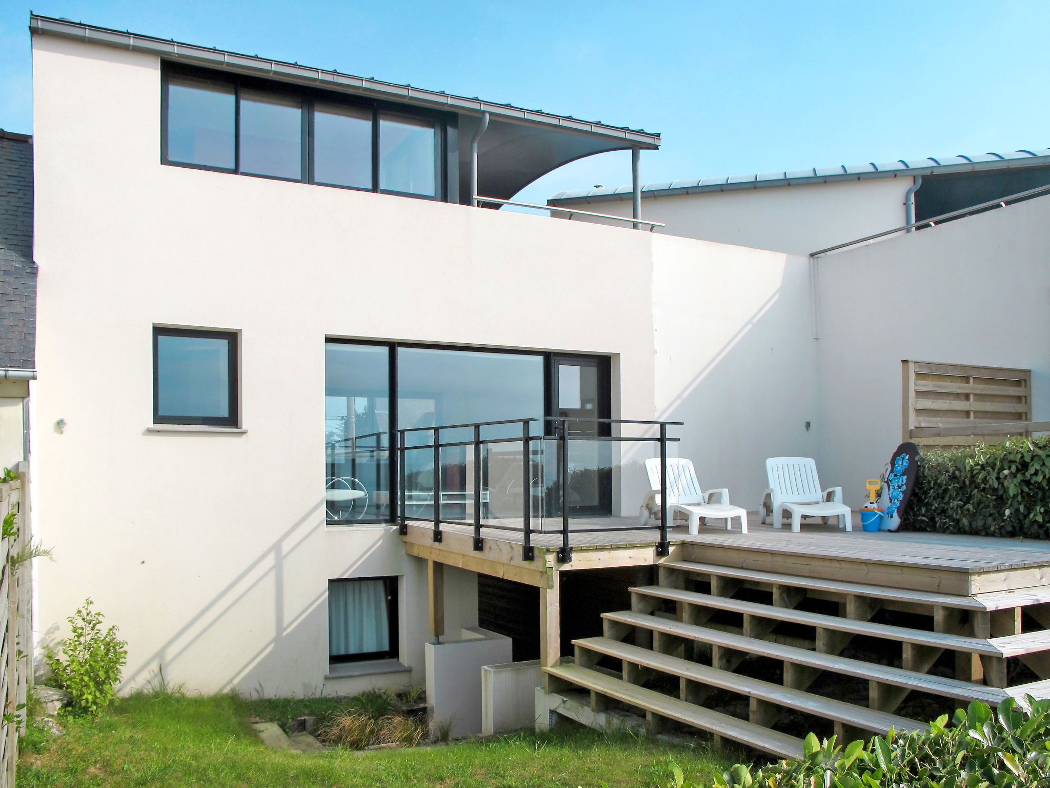 Una casa moderna de dos pisos con balcón, zona de estar al aire libre y una pequeña terraza.