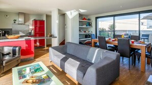 Una cocina moderna con armarios rojos, un comedor con mesa y sillas de madera, y un sofá gris.