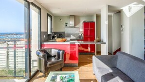 Un apartamento moderno con balcón, una cocina con armarios rojos, un sofá gris y una mesa de centro con revistas.