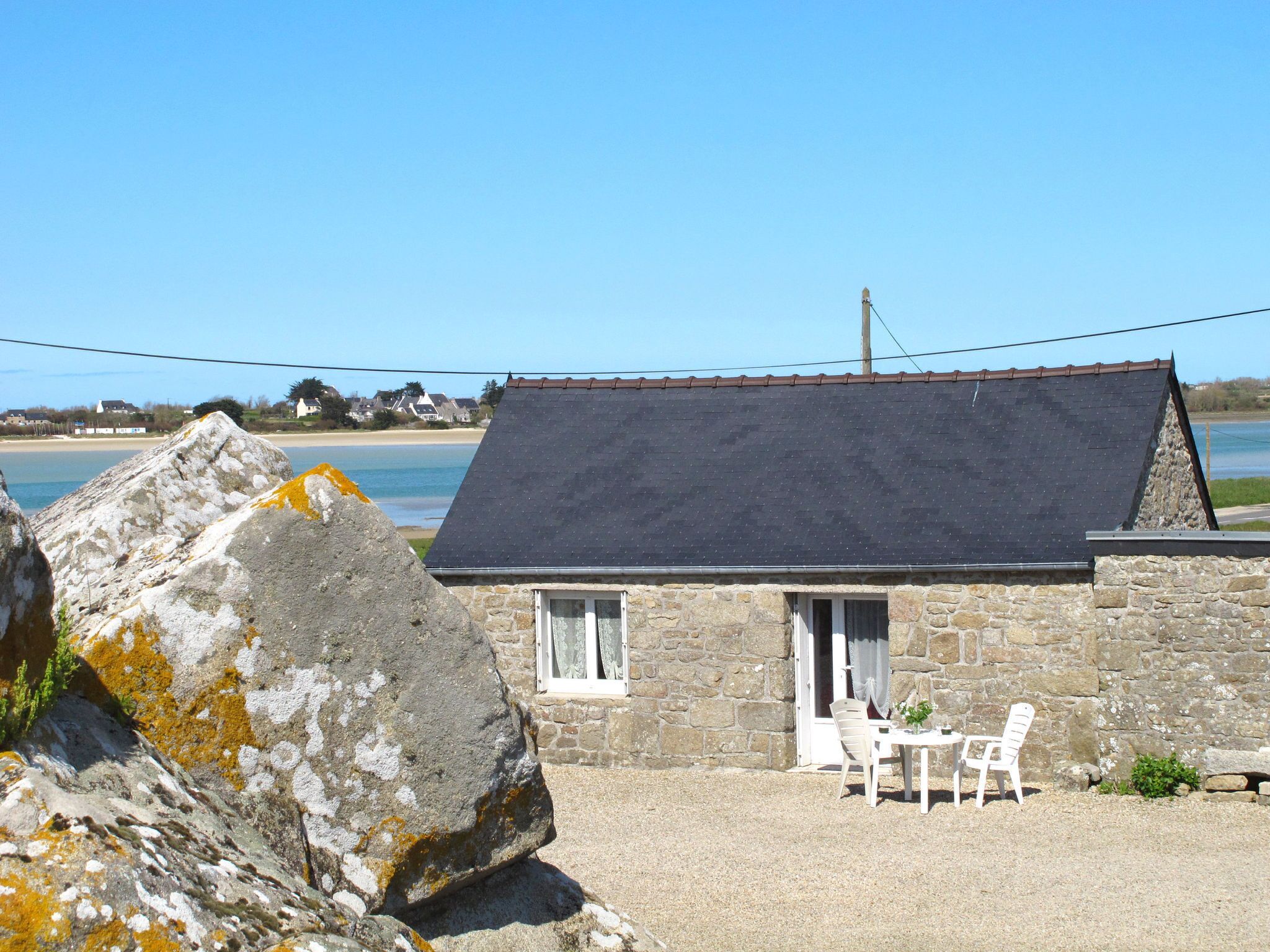 A stone cottage with a dark roof, a small porch, and a table with two chairs.