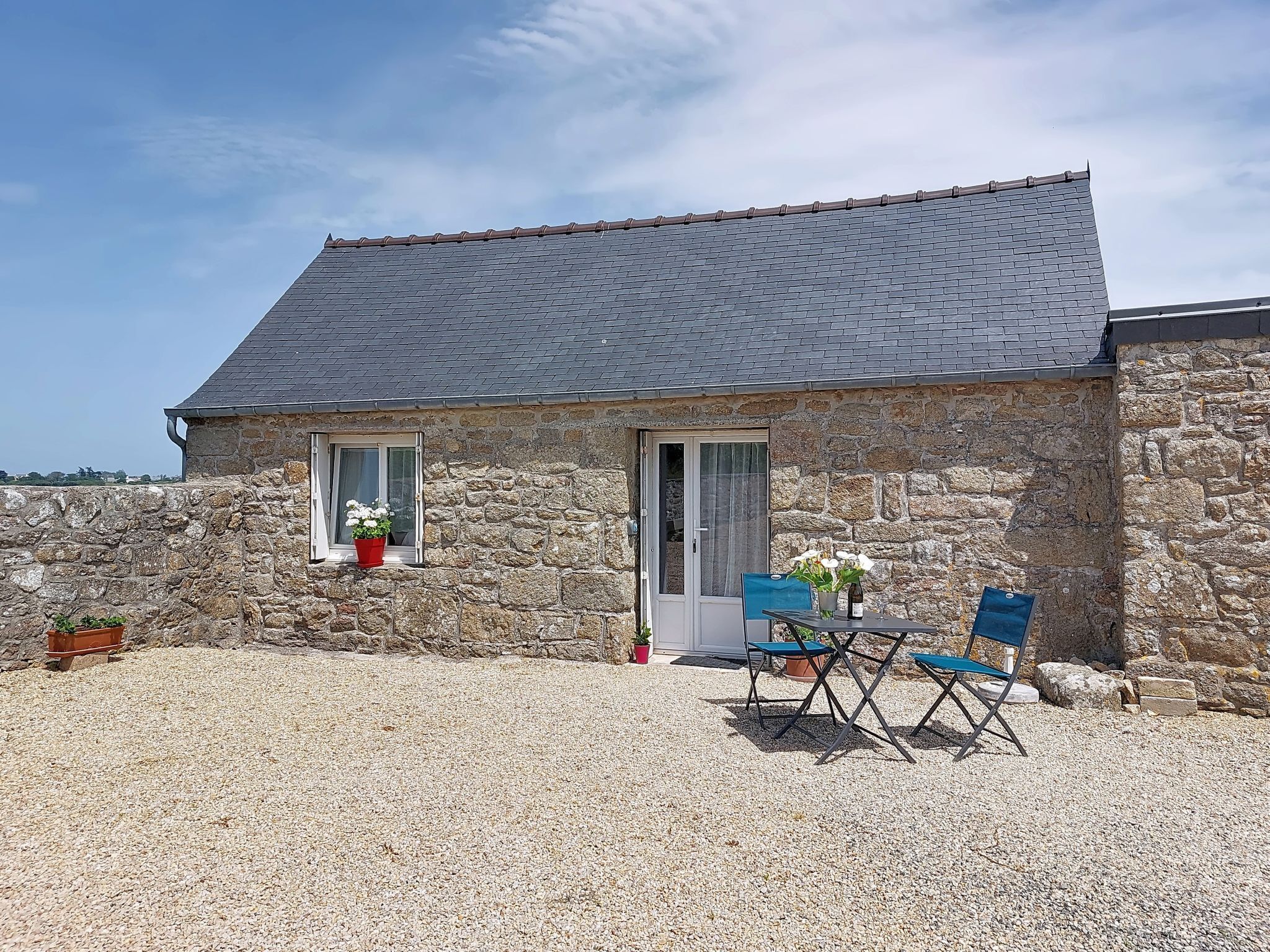 A stone building with a tiled roof, a gravel patio, and a table with chairs.