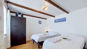 Ein Zimmer mit zwei Betten, Holzboden, einem dunklen Wandschrank und einer Decke mit sichtbaren Balken.