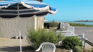 An outdoor seating area with a table and chairs, a striped umbrella, and a view of the sea. - Tal Ar Mor by Interhome (Plouescat)