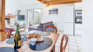 A cozy kitchen with wooden beams, a dining table with croissants, a bottle of beer, and a TV in the background. - Tal Ar Mor by Interhome (Plouescat)