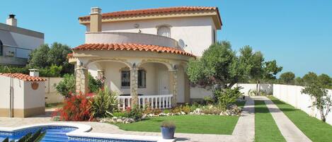 Eine mediterrane Villa mit Pool, einem gepflegten Rasen und einem Kiesweg zum Eingang.