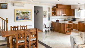A spacious living room with a wooden dining table and chairs, a kitchen with wooden cabinets and a built-in island, and a staircase leading to another level. - Vacation home Silvia by Interhome (Miami Platja)