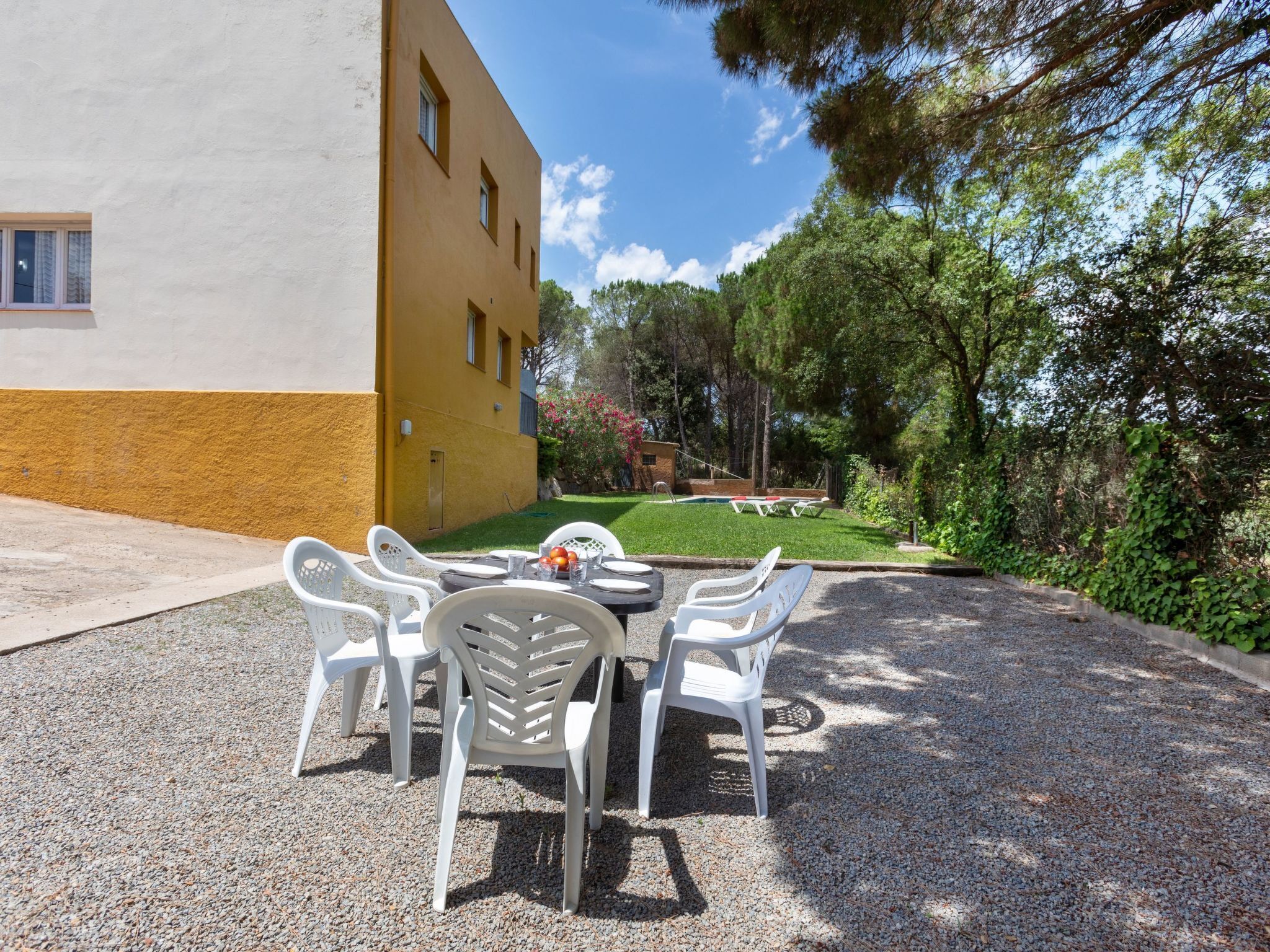 Une terrasse avec une table et des chaises, une petite piscine et un bâtiment à la façade jaune.