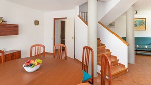 Ein Essbereich mit einem Holztisch und Stühlen, einer Obstschale, einem Holzschrank und einer Treppe zu einer oberen Ebene.