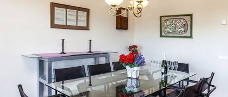 A dining area with a glass table, black chairs, a vase with flowers, a bottle of wine, and a chandelier.