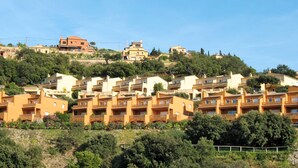Un quartier résidentiel situé sur une colline, avec des maisons à étages et des balcons, sous un ciel d’un bleu éclatant.