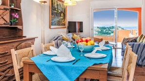 Un coin repas avec une nappe bleue, des chaises en bois, un buffet et un tableau accroché au mur.
