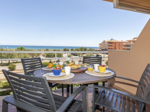 A round table with chairs on a balcony overlooking a beach.