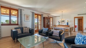 Een ruime woonkamer met leren banken, een glazen salontafel, en een eetgedeelte met een houten tafel en stoelen.