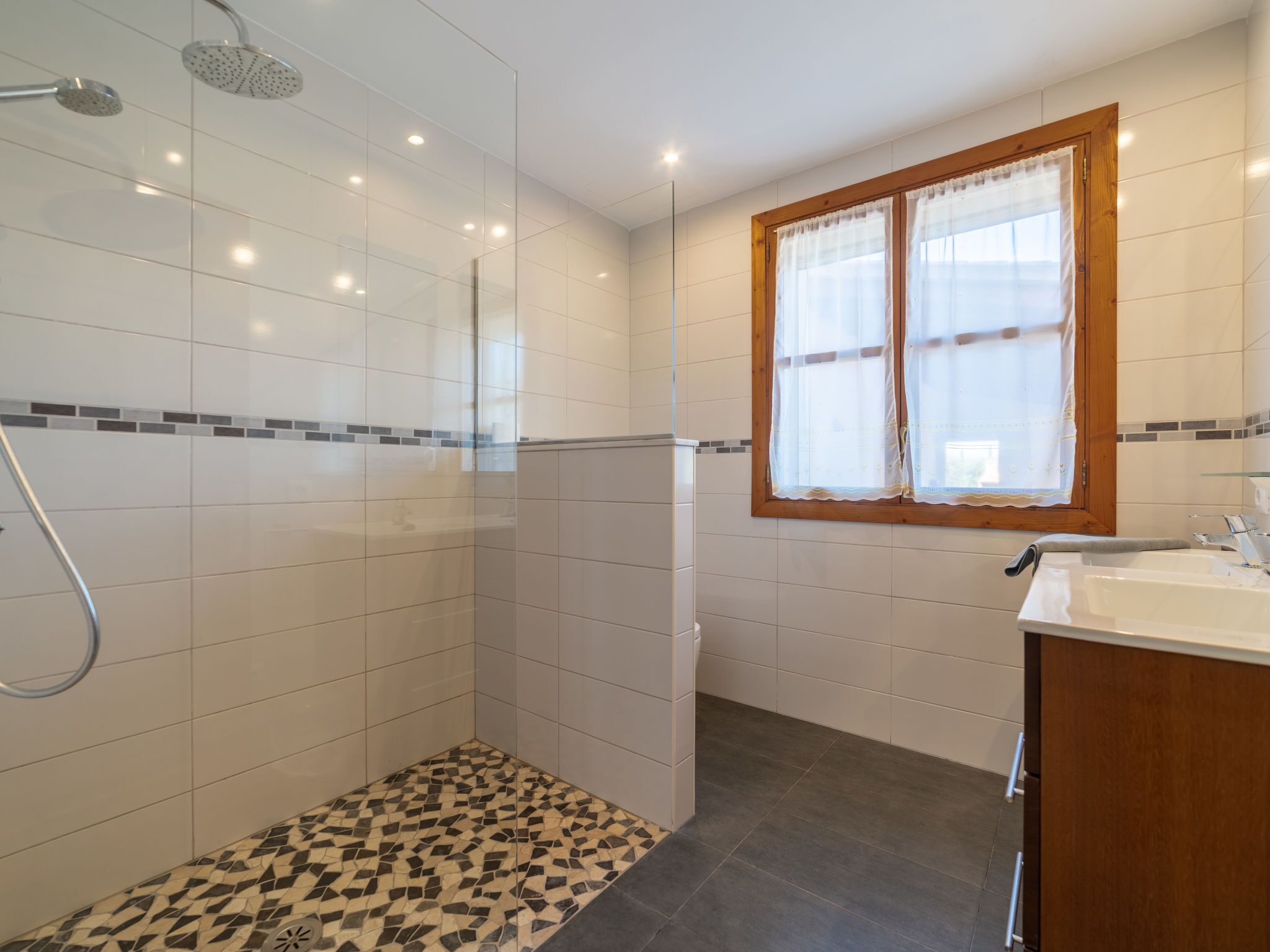 A modern bathroom with a shower, a sink, and a window with curtains.