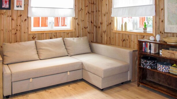 A wooden-paneled room with a beige sectional sofa, two windows with white blinds, a bookshelf, and a map on the wall.