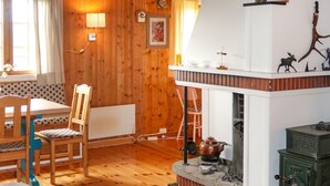 A cozy room with wooden walls, a fireplace, a dining table with chairs, and a window with curtains.