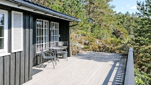 Ein Holzhaus mit einer Terrasse, Sitzgelegenheiten im Freien und Blick auf einen bewaldeten Bereich.
