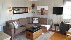 Ein Wohnzimmer mit Ecksofa, Couchtisch aus Holz, Flachbildfernseher und Fernsehschrank.