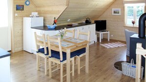 A cozy attic-style room with a wooden ceiling, a dining table with chairs, a small kitchen area with a refrigerator, a television, and a fireplace. - Vardeheii by Interhome (Arnafjord)