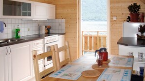 A wooden interior with a kitchen featuring white cabinets, a stove, and a window overlooking a body of water. - Vardeheii by Interhome (Arnafjord)