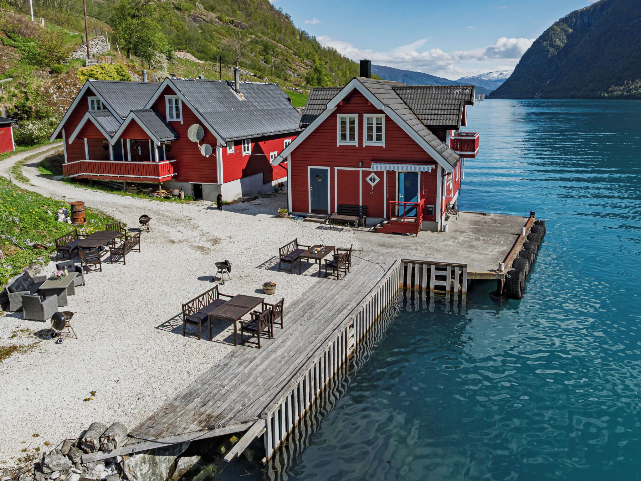 Une jetée en bois mène à une rangée de bâtiments rouges dotés de terrasses et offrant une vue dégagée sur l’eau.
