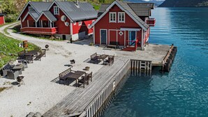 A wooden pier leading to a row of red buildings with outdoor seating and a clear view of the water. - Vardeheii by Interhome (Arnafjord)