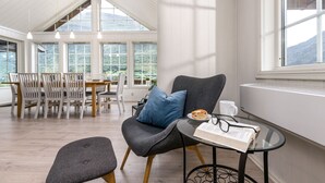 Un cuarto acogedor con comedor, un rincón de lectura con una silla y una mesa, y ventanas amplias que ofrecen vistas al exterior.