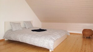 Une chambre avec un plafond en pente, un lit avec une literie à motifs, deux oreillers et une petite chaise en osier.