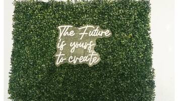 A wall with a green hedge and a sign that reads "The Future is yours to create."
