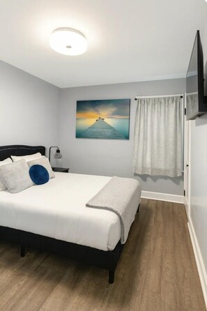 Ein Schlafzimmer mit einem Bett, einem Nachttisch, einer Lampe, einem Gemälde und einem Vorhang.