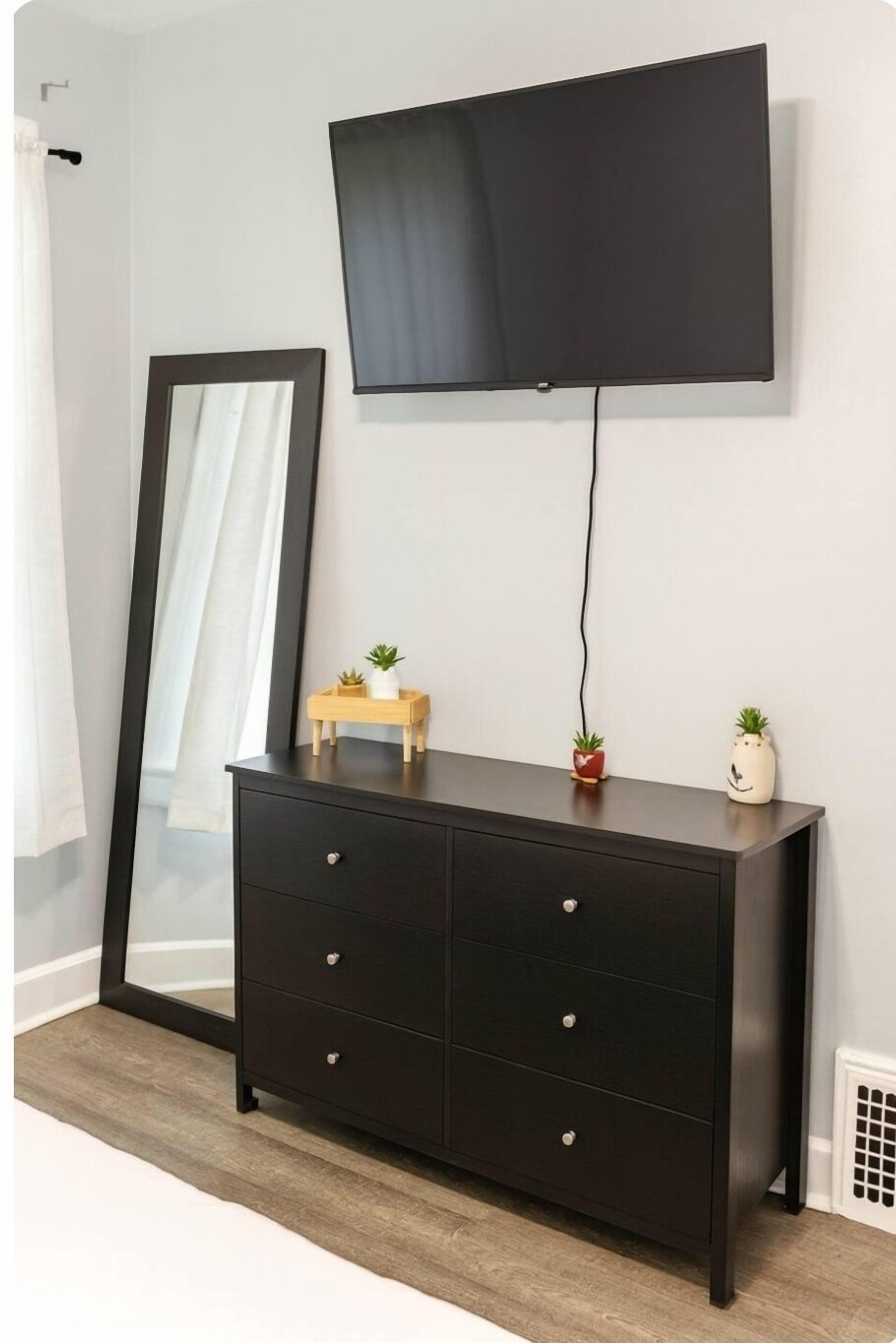 A dark wooden dresser with drawers, a flat-screen TV mounted above it, and two small potted plants on the dresser.