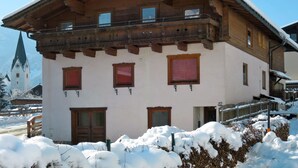A traditional wooden chalet with a balcony, multiple windows, and a snow-covered landscape.