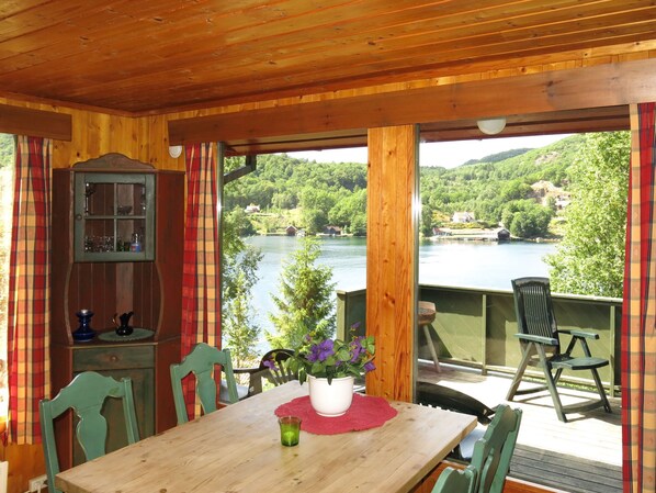 A wooden dining area with a table, chairs, and a view of a lake surrounded by greenery.