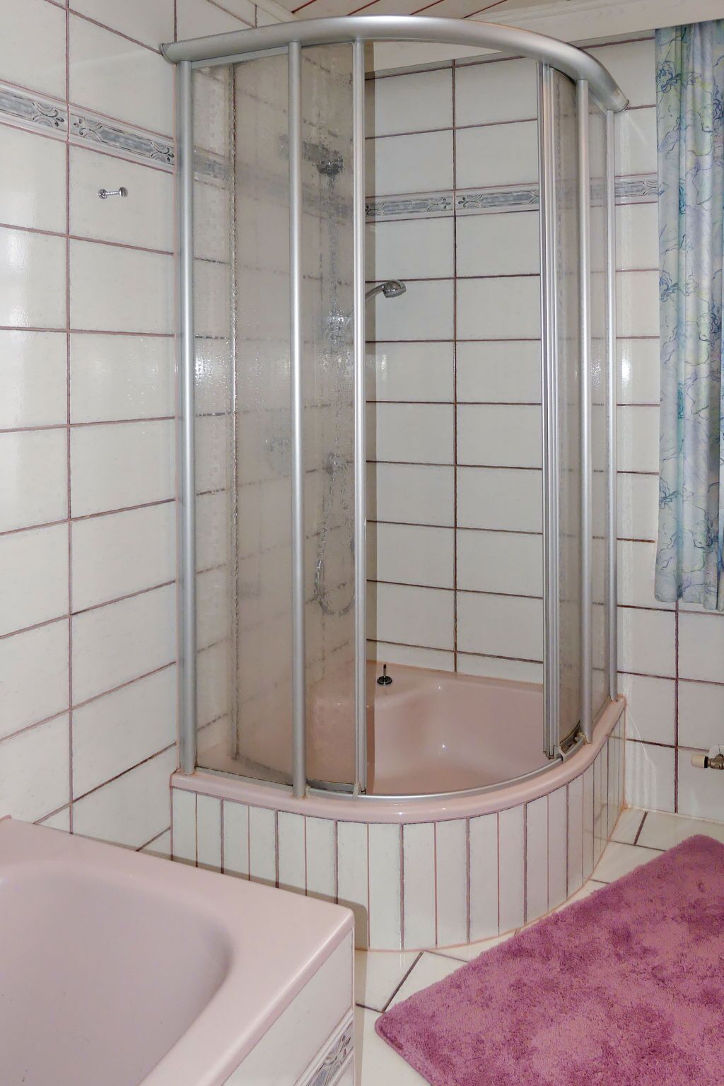 Une cabine de douche avec une porte en verre, une baignoire et un tapis de bain violet.