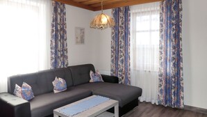 Een woonkamer met een donkere bank, gestreepte kussens, een houten salontafel en een hanglamp.