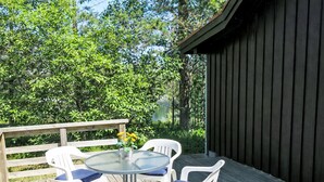 Une terrasse en bois avec une table ronde en verre et quatre chaises blanches dotées de coussins bleus.