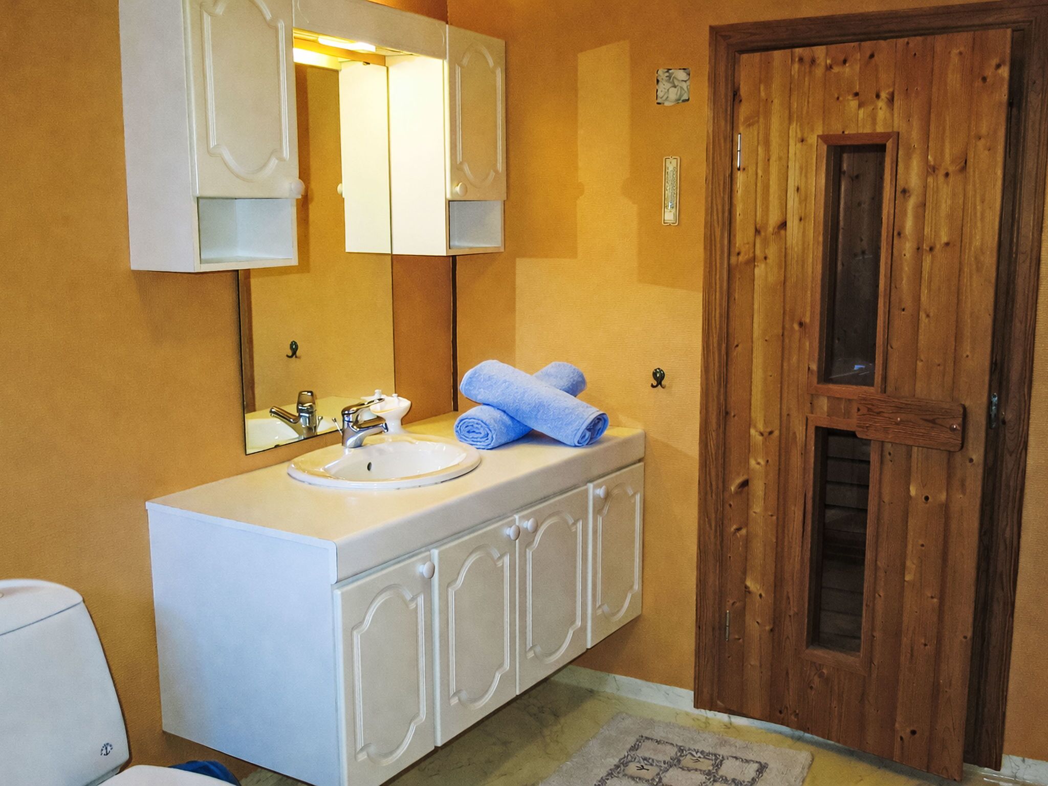 Casa de banho com lavatório branco, espelho e porta de madeira.