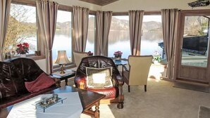 Une pièce chaleureuse avec un canapé en cuir, une table basse en bois et une vue sur un lac, visible à travers de grandes fenêtres.