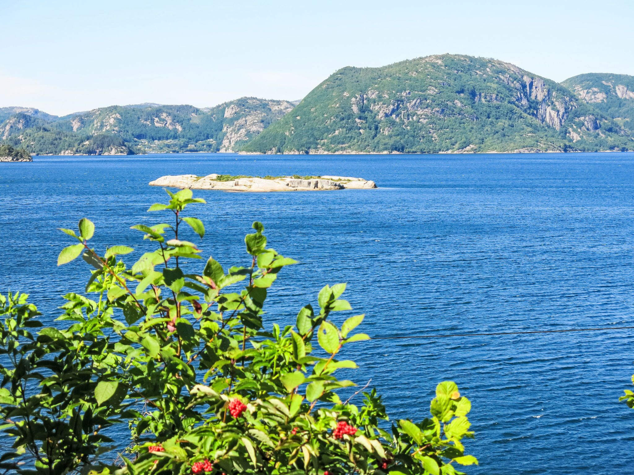 Une vue sur la côte, avec une mer bleue et limpide, une petite île et des collines verdoyantes en arrière-plan.