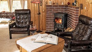 Une pièce chaleureuse avec des fauteuils en cuir, une cheminée et une table sur laquelle se trouvent un livre et un verre de vin.