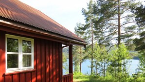 Une cabane rouge, surmontée d’un toit en métal, qui surplombe un lac entouré d’arbres.