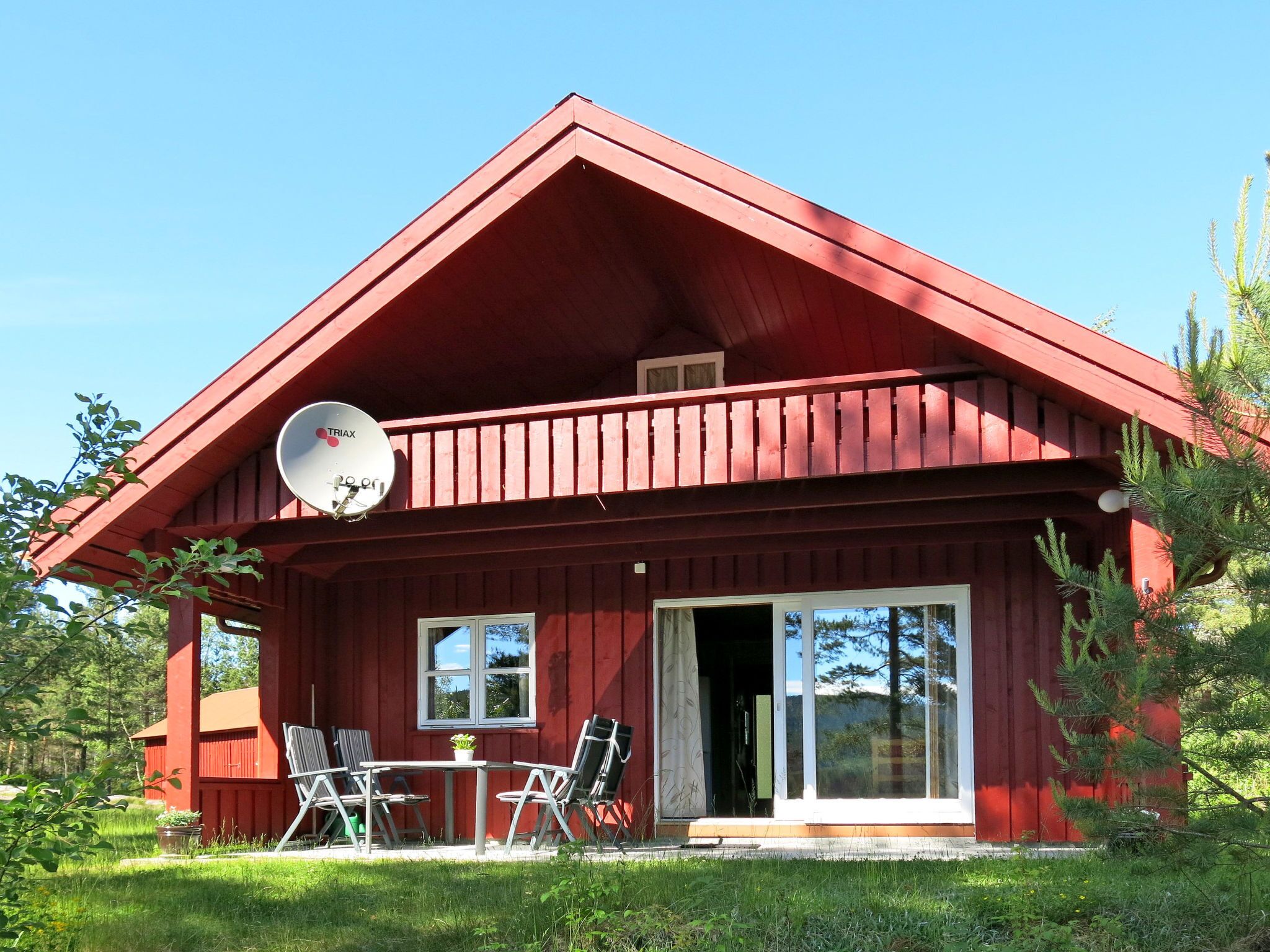 A red wooden cabin with a satellite dish, a sliding glass door, and a patio with outdoor seating.