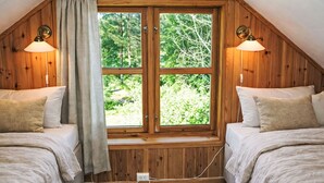 Une chambre avec deux lits, une grande fenêtre, des murs en bois et deux lampes fixées au mur.