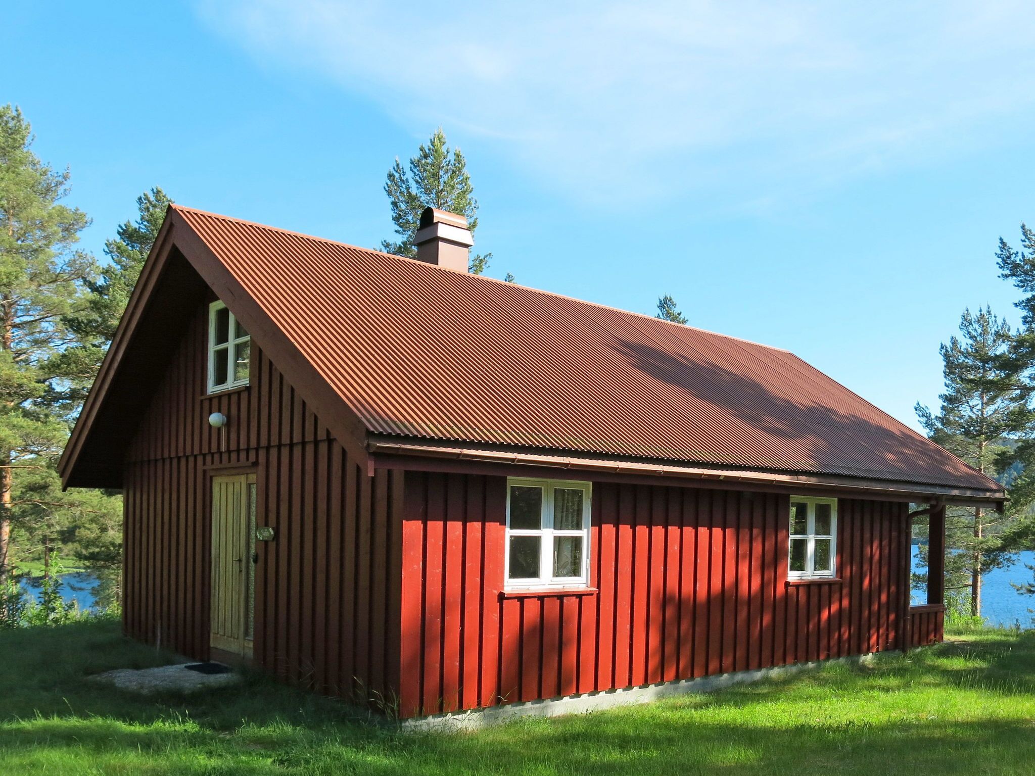 Une cabane en bois rouge, avec un toit à pignon, une cheminée et un petit porche.
