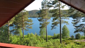 Une vue depuis une terrasse en bois donnant sur un lac, entouré d’arbres et de collines.